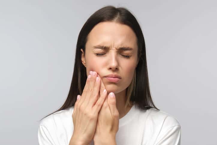 A woman holding her face in pain due to a dental emergency. 
